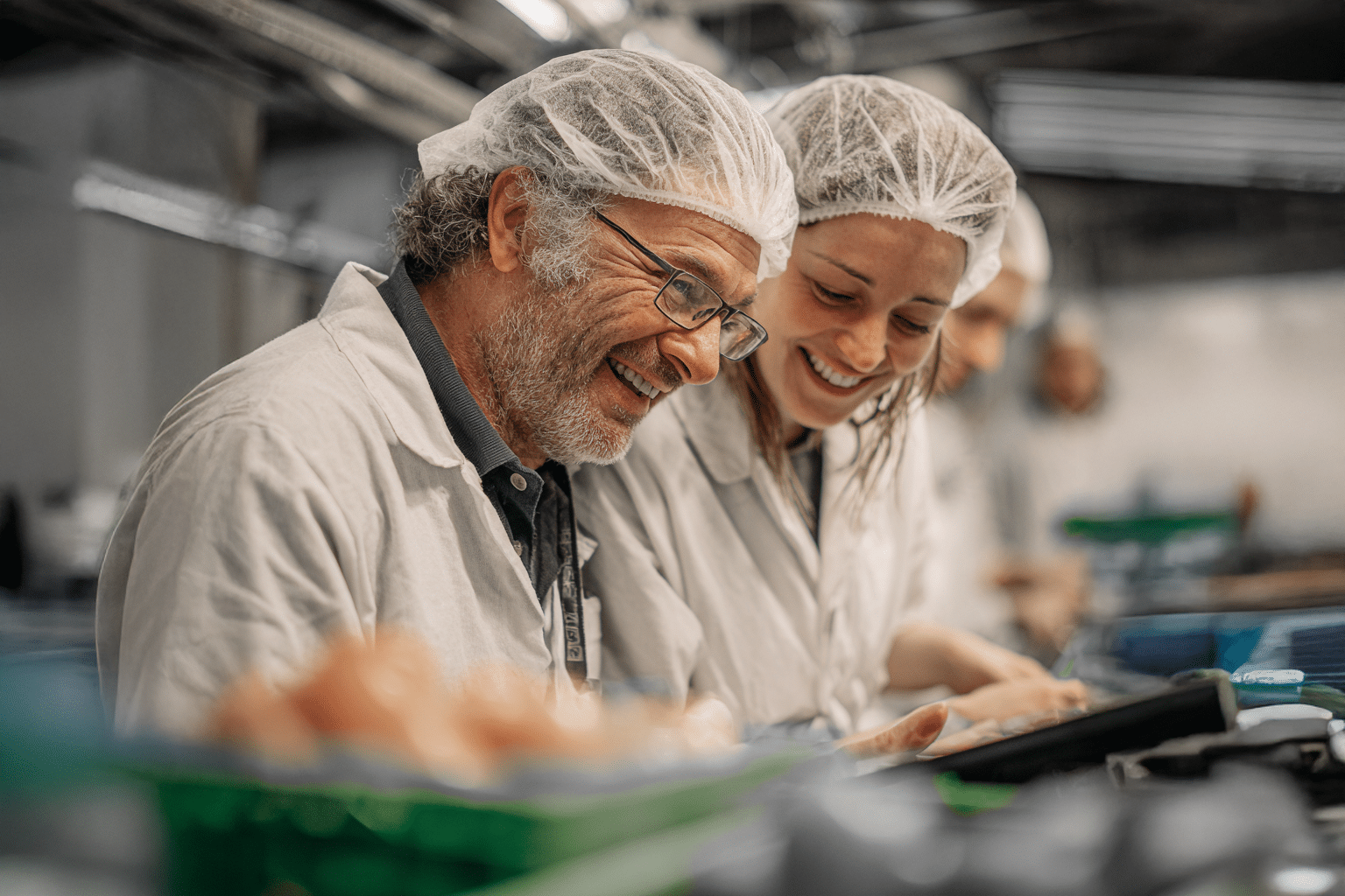 Deux employés de l’agroalimentaire souriants en tenue de protection, travaillant côte à côte sur une ligne de production – illustration de la fidélisation et du bien-être au travail.